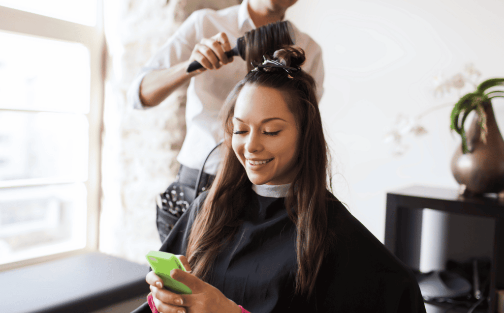 hair dresser styling clients hair while client texting on social media