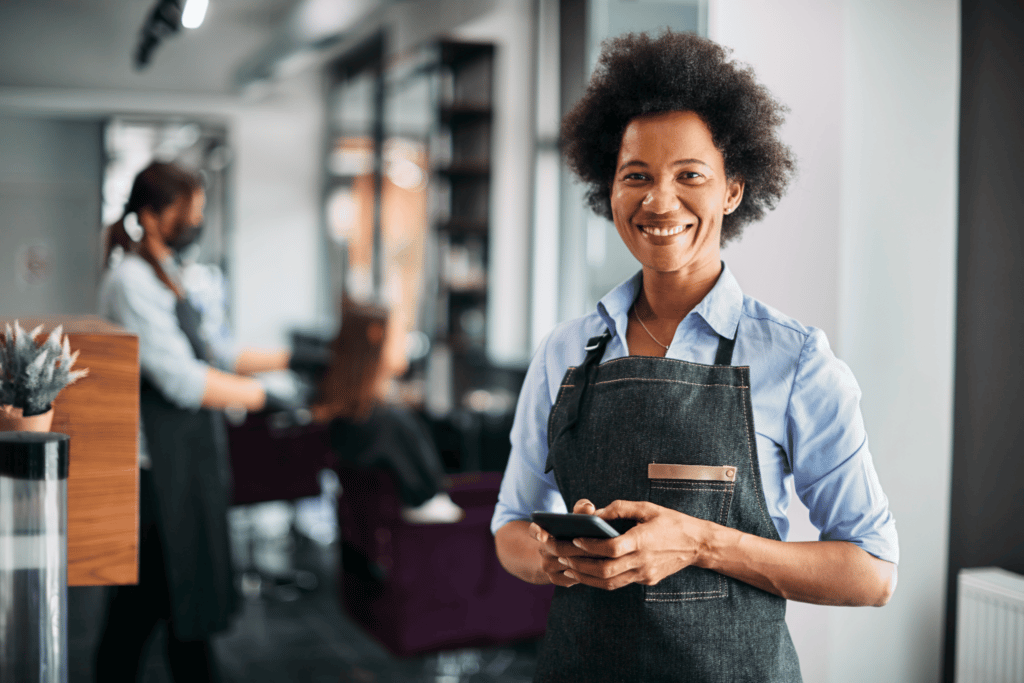 hair stylist using phone in a hair salon with other professional on the background