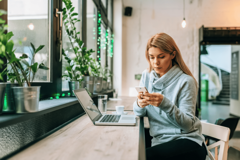 woman checking phone while working on a laptop and cafe