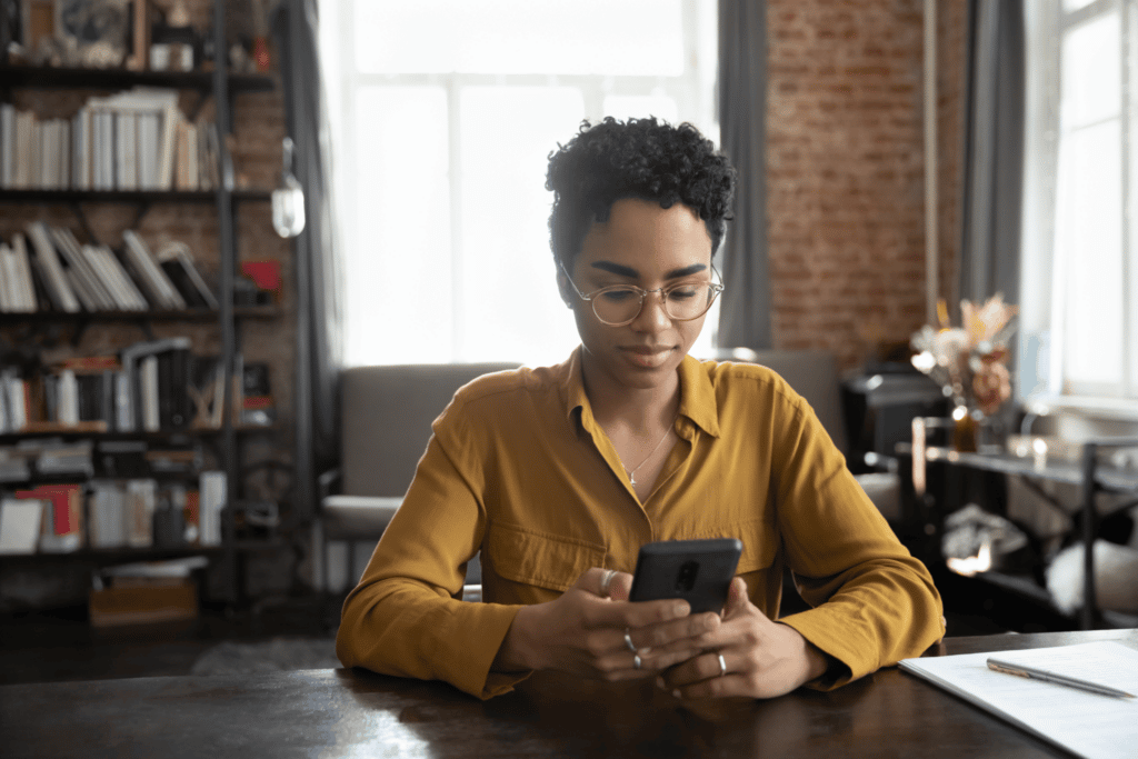woman receiving sms marketing on mobile on orange clothes with window behind