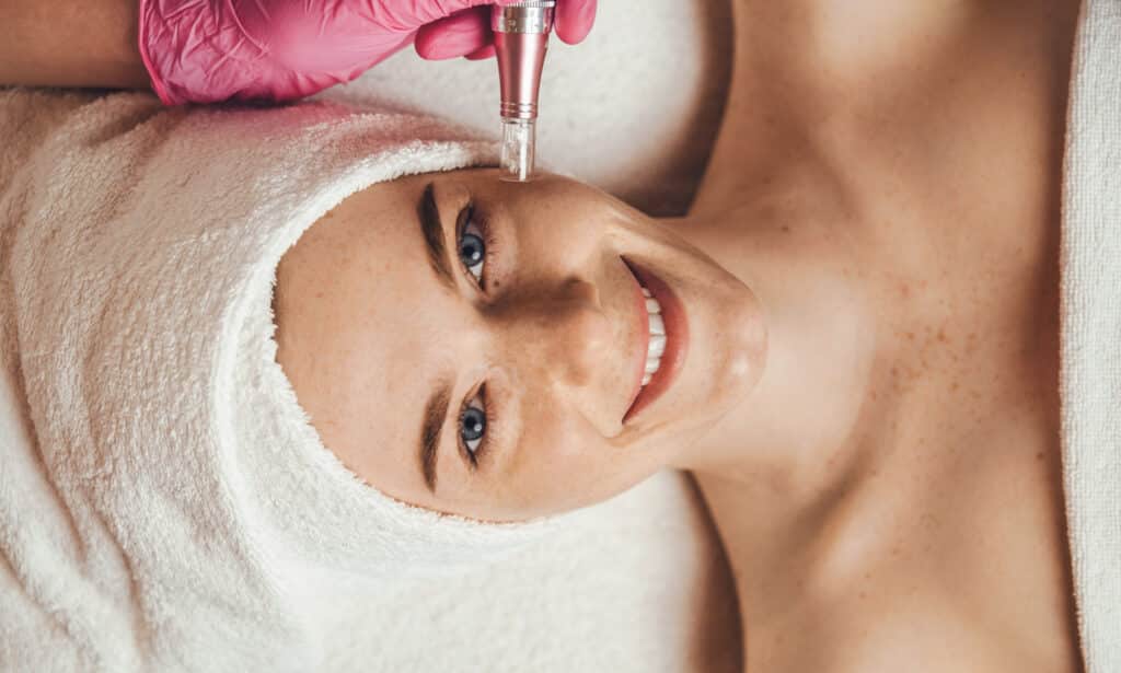 esthetician client smiling receiving microdermabrasion procedure in a beauty spa salon.