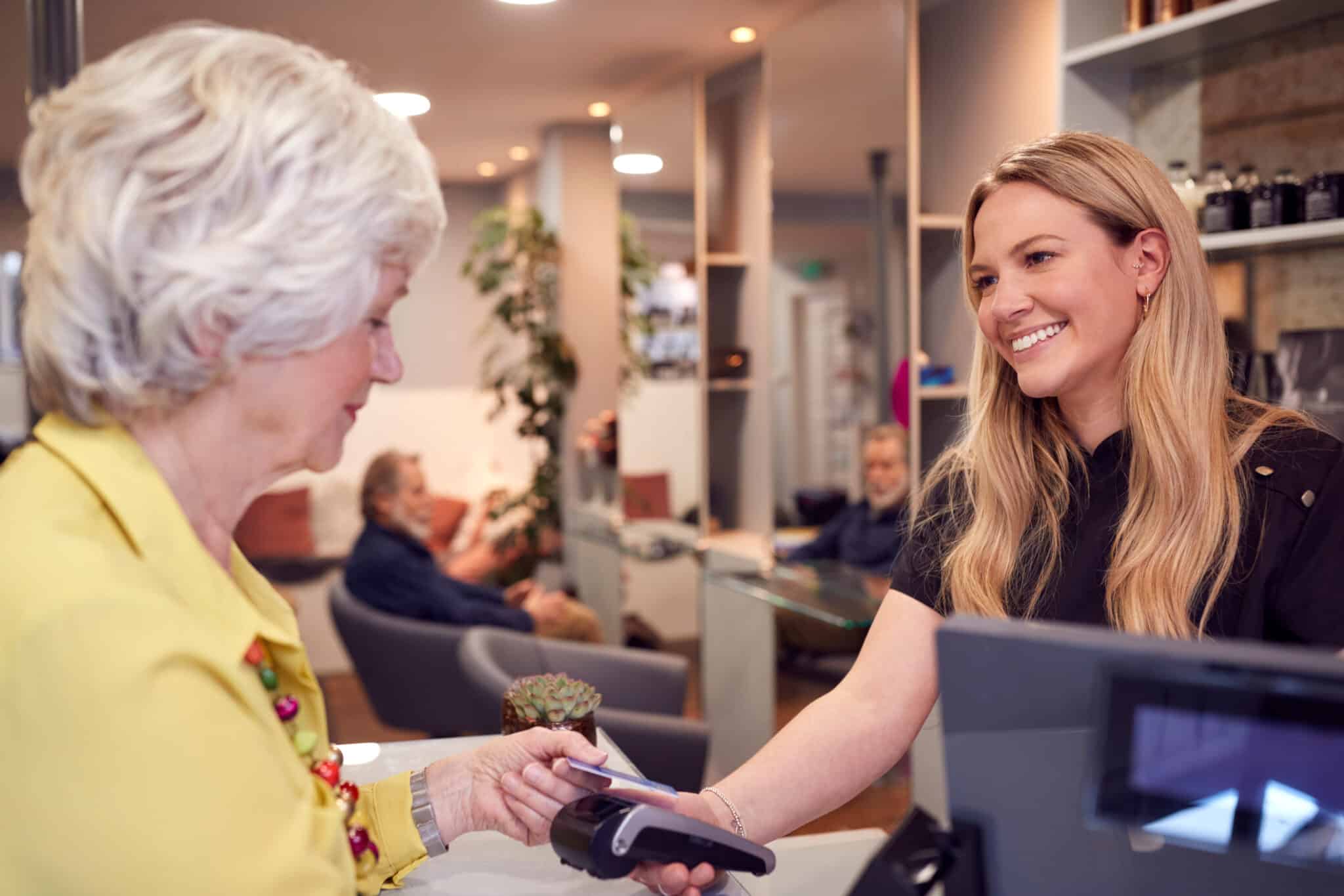 woman paying hair salon stylist with other clients in the background