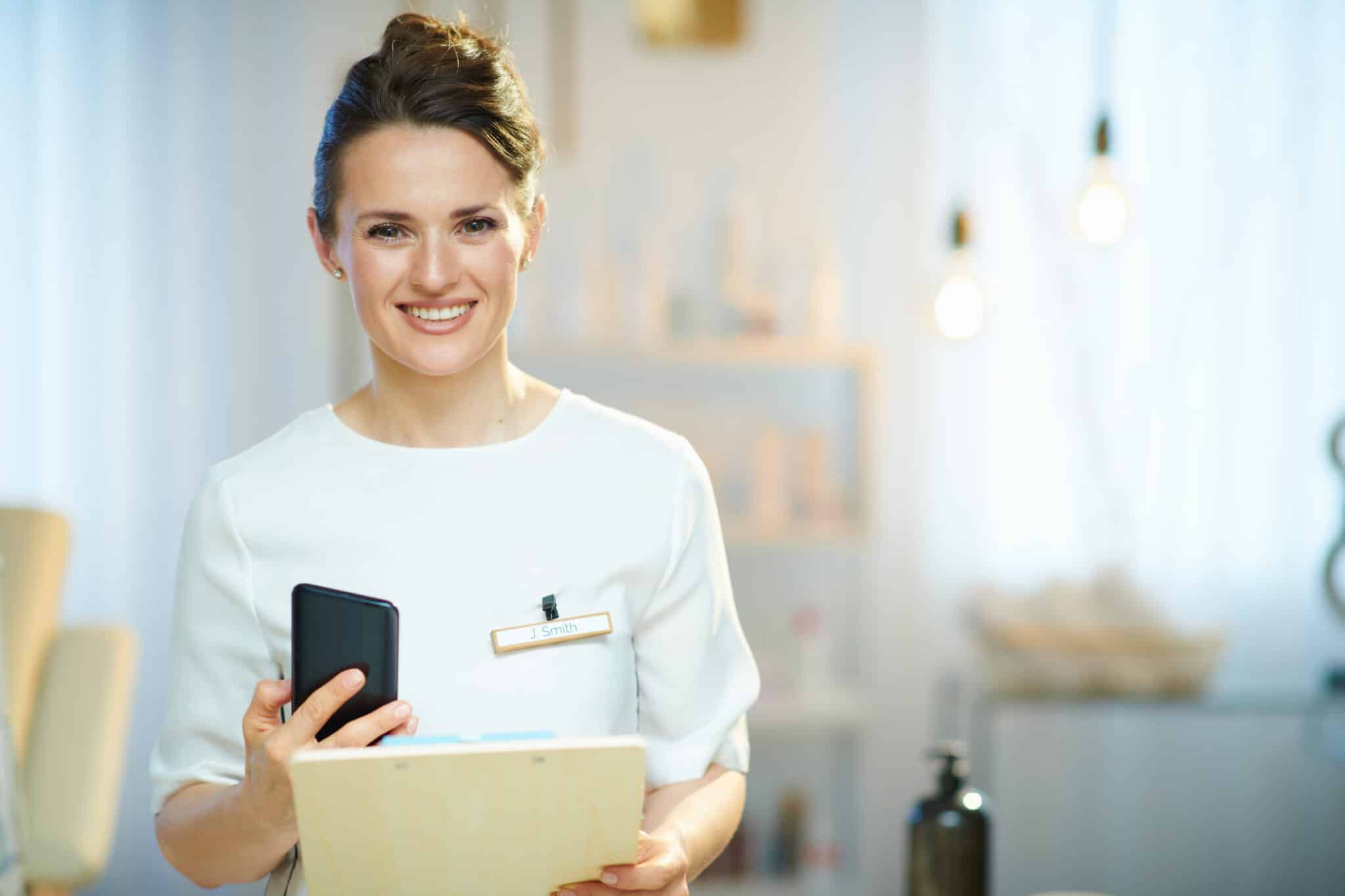smiling woman worker with clipboard in modern beauty salon sending sms marketing massages