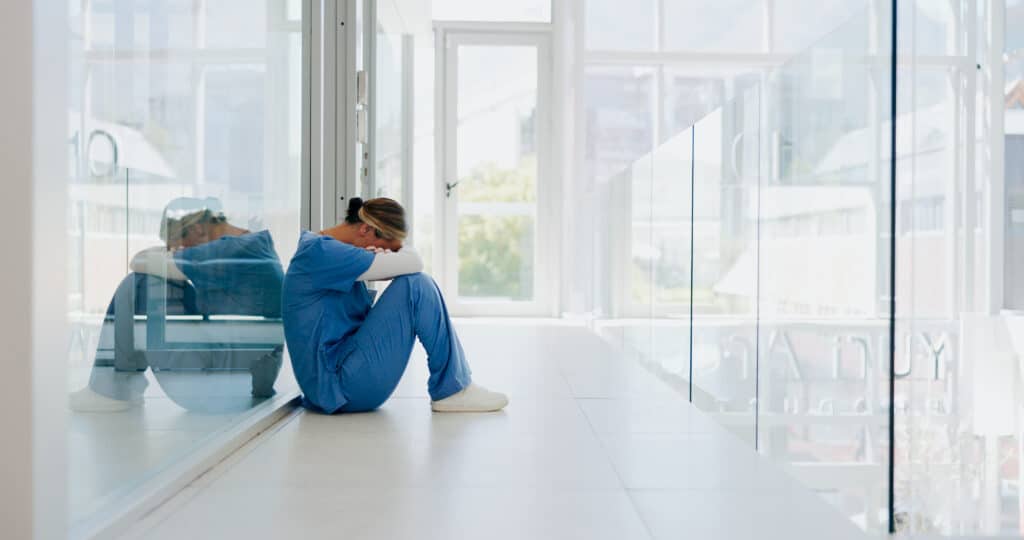health professional sitting on the floor with hands around the head as a sign of burnout
