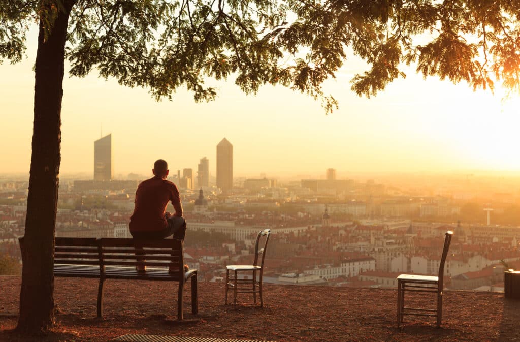 man sitting on a bench watching the sunrise over a city