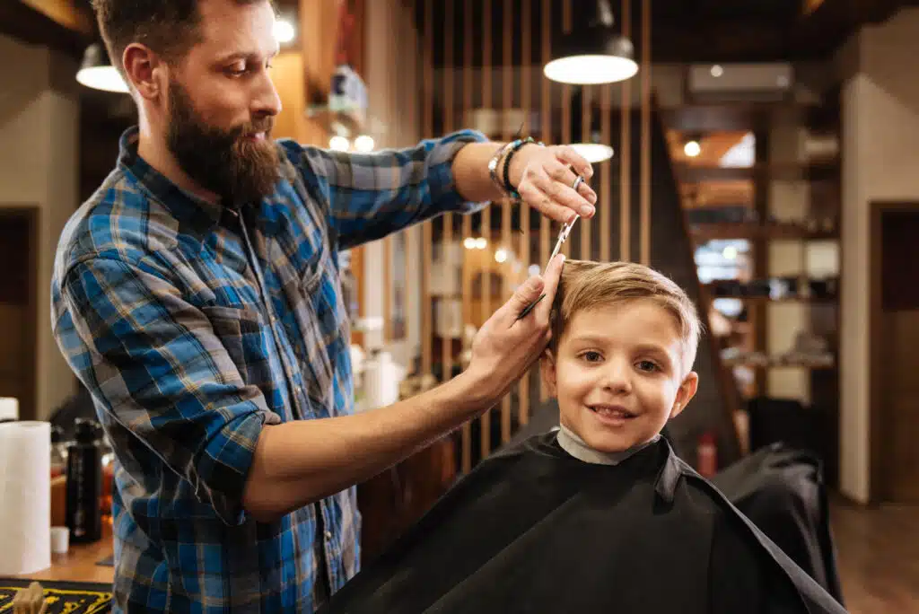 hairdresser cutting kids hair with scissor while kids smiles